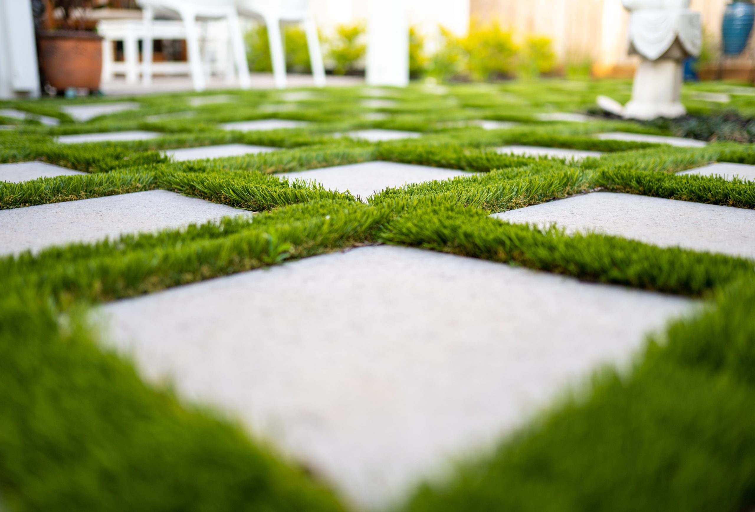 Geometric pattern of square concrete pavers set in green grass, photographed at ground level in a backyard or garden setting.